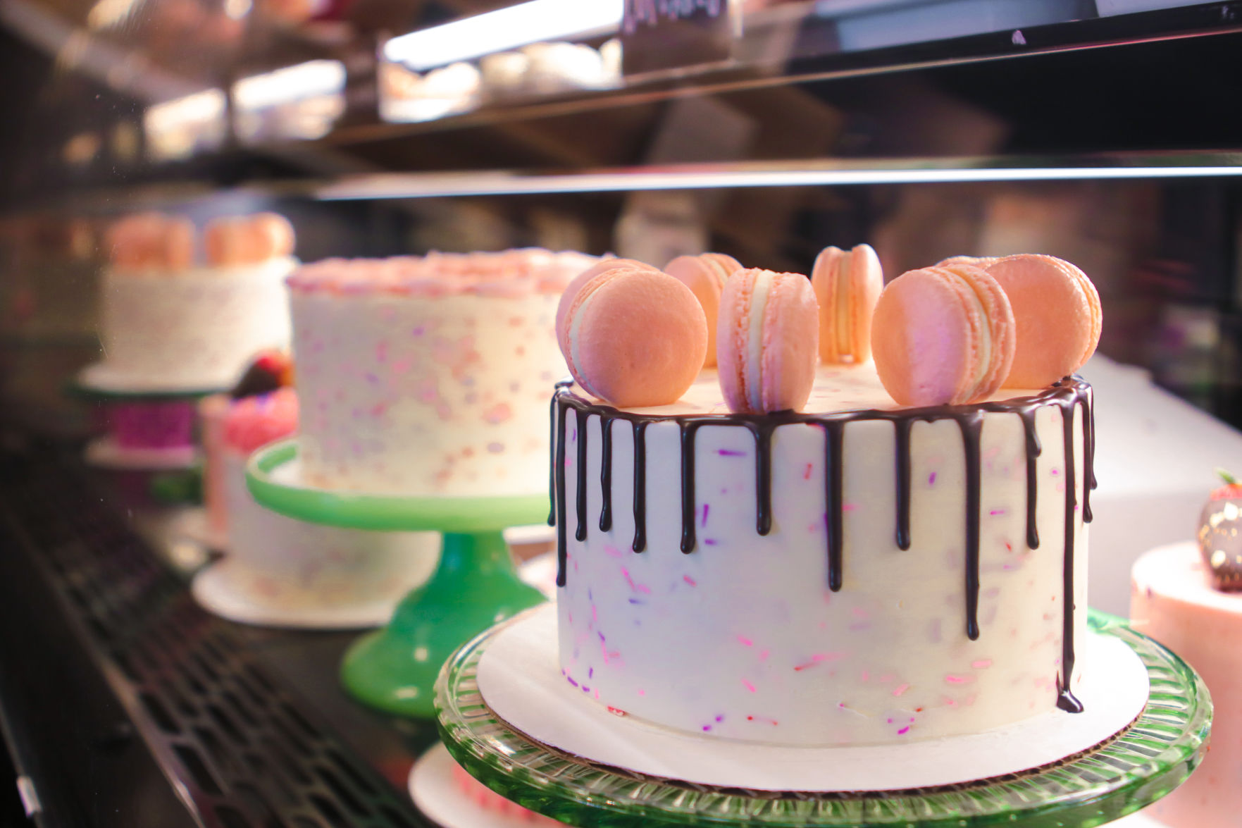 A line of cakes with toppings such as macarons sits in a display case.